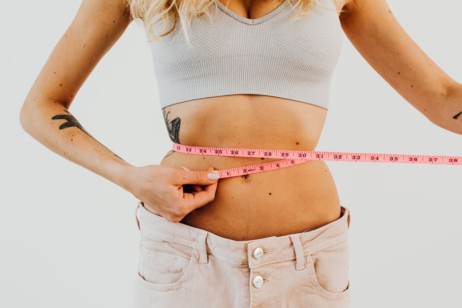 Person measuring their waist with tape measure tracking weight loss progress